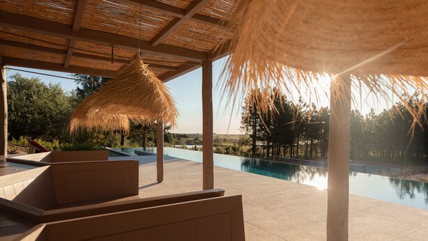 Una piscina infinita con vistas al paisaje, asientos en terraza de madera y una estructura de techo de paja.
