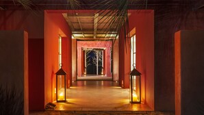 Un pasillo con paredes rojas y suelo de piedra, que lleva a una puerta con silueta de árbol.