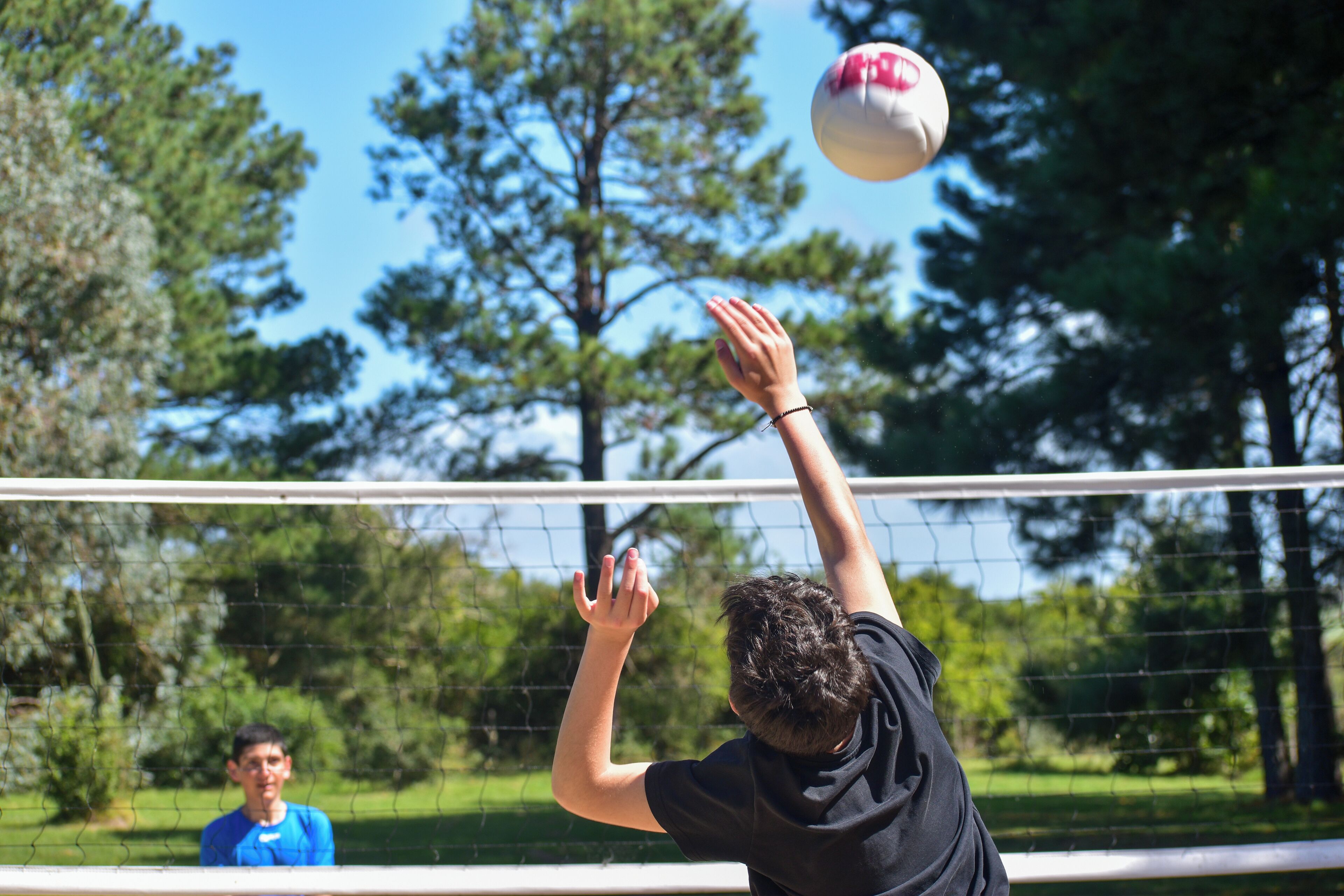 Una persona jugando voleibol en una cancha con una red, rodeada de árboles y vegetación.