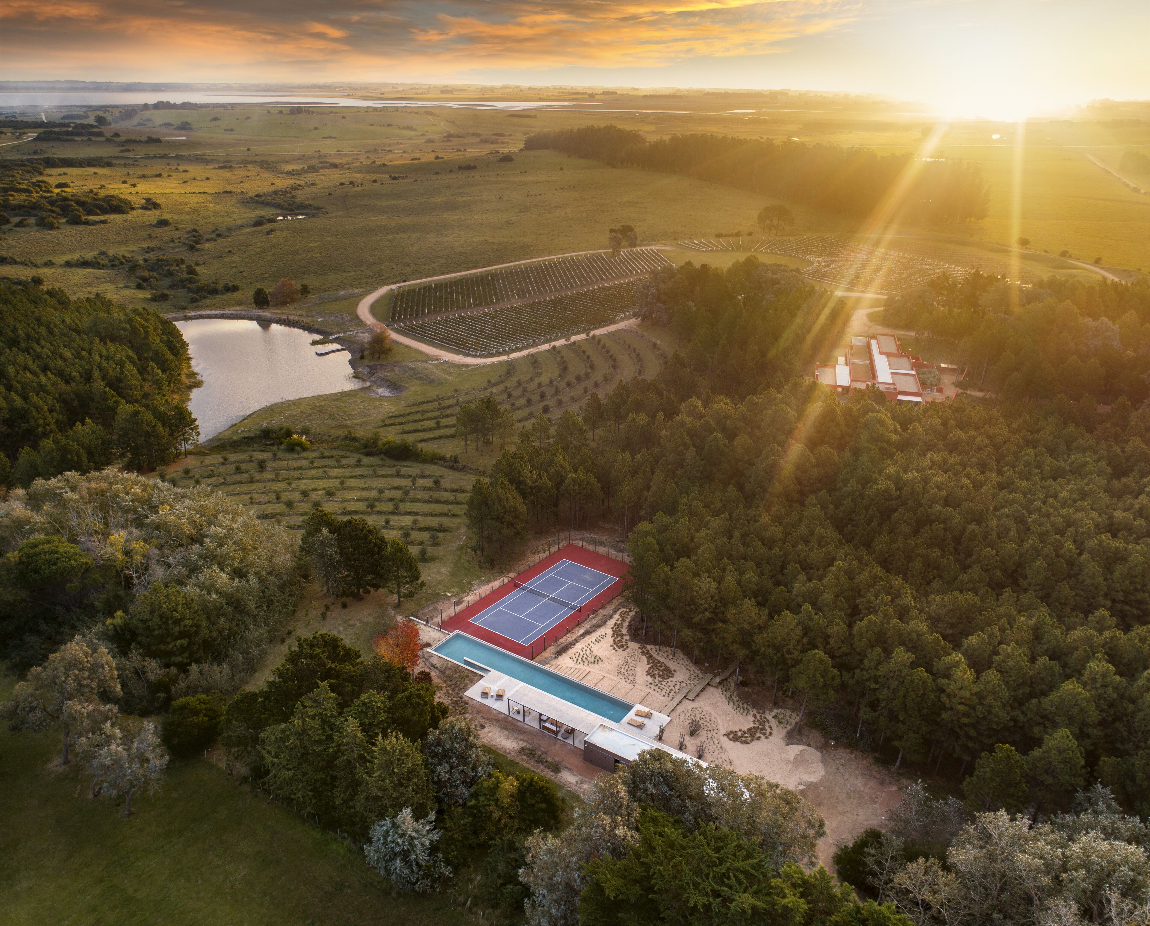 Vue aérienne d’une propriété dotée d’un court de tennis, d’une piscine et d’une grande étendue d’eau.