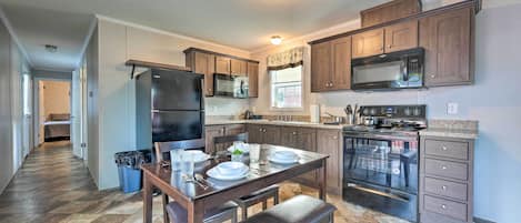 A modern kitchen with a built-in oven, microwave, and refrigerator. There is a dining table with chairs and a bench.