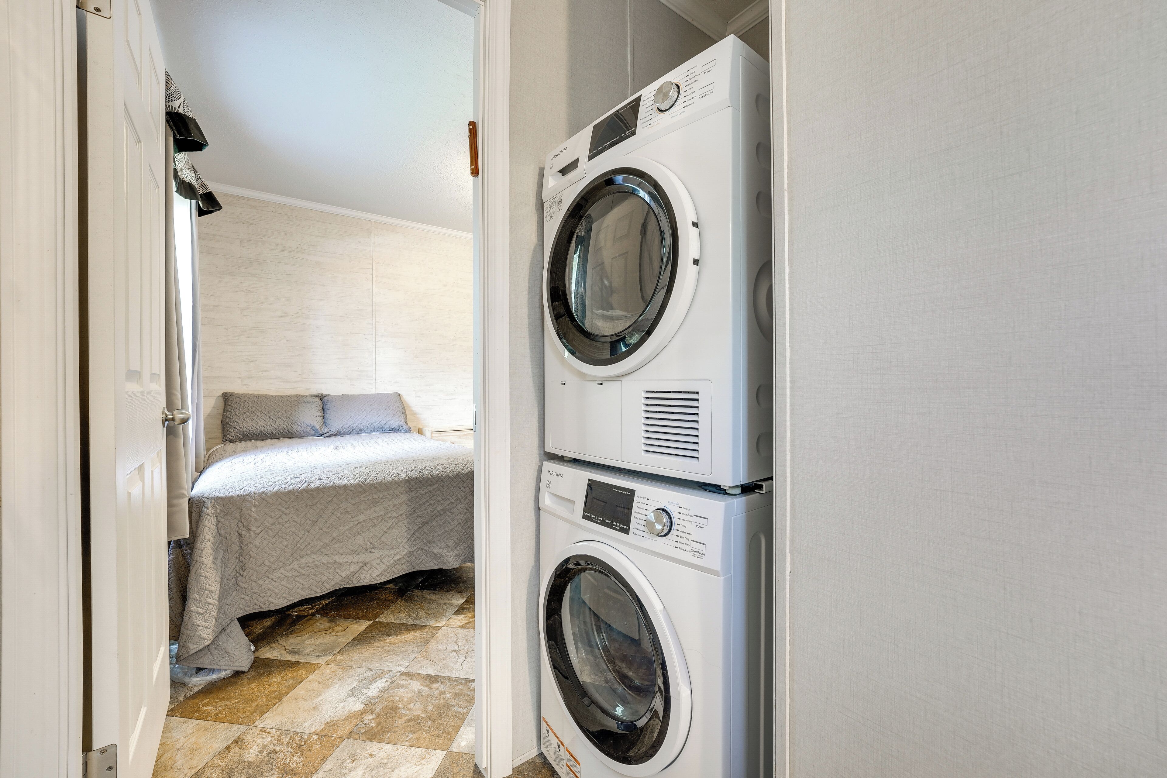 A laundry room with two stacked washing machines and a bed with a white cover.