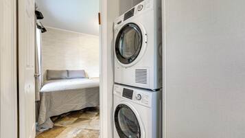 A laundry room with two stacked washing machines and a bed with a white cover.