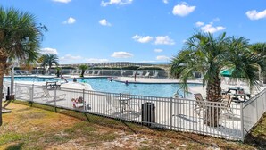 Un área de piscina con terraza cercada, sillas de descanso y palmeras.