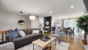 A modern living room with a sofa, armchairs, a coffee table, and a dining area with a chandelier. - Heart of Pocono Mountains - Huge Yard - Game Rm <10 min to Kalahari & Casino (Mount Pocono)