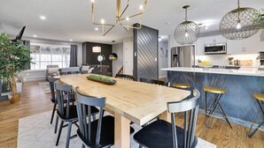A modern kitchen with a wooden dining table, bar stools, and pendant lights. - Heart of Pocono Mountains - Huge Yard - Game Rm <10 min to Kalahari & Casino (Mount Pocono)