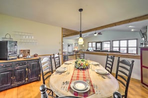Un comedor con una mesa de madera dispuesta para cuatro personas, rodeada de sillas. Se ve una cocina al fondo con un refrigerador y un microondas.
