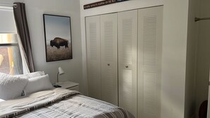 Een slaapkamer met een bed, kussens, een bedlampje, een lijst met een bison afbeelding en een set gesloten luiken.
