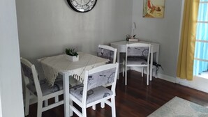 Een eetruimte met een ronde wandklok, een tafeltje met een plant en stoelen met kussens in nautische stijl.