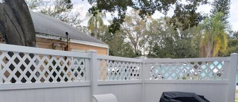 Une terrasse avec trois chaises en métal blanc, un barbecue noir et une clôture en treillis blanc.