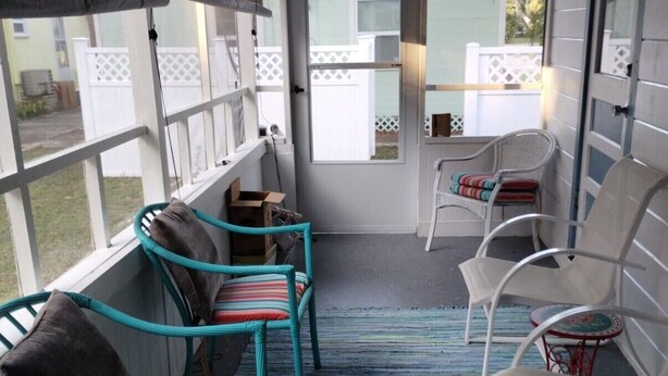 Een veranda met vier stoelen, een tafeltje en uitzicht op een witte schutting en groen.