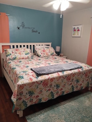 A bedroom with a bed, floral bedspread, and a wall with a motivational quote.