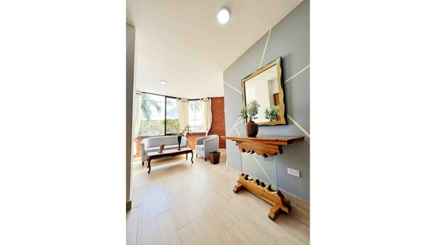 A modern living room with a sofa, armchairs, a wooden coffee table, and a large mirror on the wall. - Modern Apt With View of the Basilica (Guadalajara de Buga)