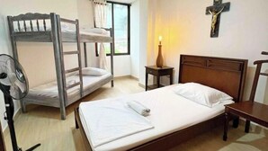 A dormitory room with bunk beds, a single bed, a fan, a nightstand, and a wall-mounted cross. - Modern Apt With View of the Basilica (Guadalajara de Buga)