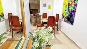 A dining area with a wooden table and chairs, a vase with white flowers, and a colorful painting on the wall. - Modern Apt With View of the Basilica (Guadalajara de Buga)