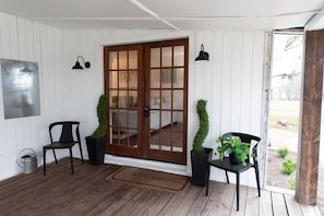 A porch with a wooden floor, a welcome mat, two chairs, a door with glass panels, and a wall-mounted sign. - Charming 3/2 Farmhouse Near Fixer Upper and Gathering Oaks (Crawford)