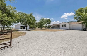 A residential area with a gravel driveway, a white garage, and a small white building with an open door. - Charming 3/2 Farmhouse Near Fixer Upper and Gathering Oaks (Crawford)