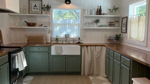 Een keuken met groene kastjes, een betegelde vloer, een raam met uitzicht en een hangende lamp.
