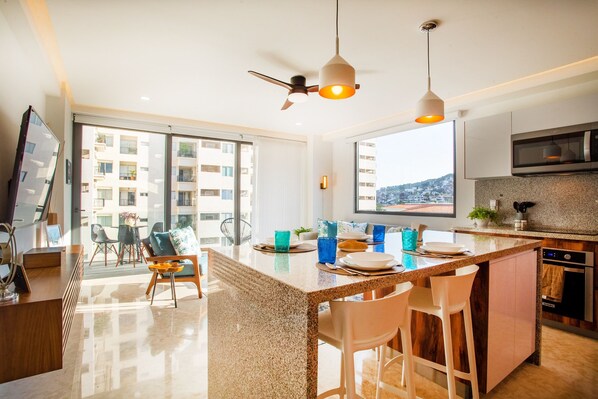 A modern kitchen with a large island, a dining area with chairs, and a view of the city through large windows.