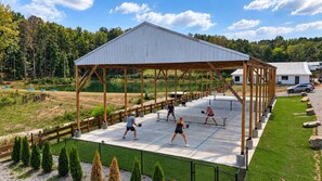 Un court de tennis extérieur doté d’un pavillon abrité, entouré d’une clôture et de verdure.