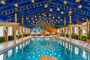An indoor swimming pool with a ceiling adorned with hanging lights, wooden beams, and a tropical mural in the background.