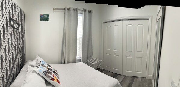 A bedroom with a bed, a wardrobe, a window with curtains, a wall with a street sign, and a towel rack.