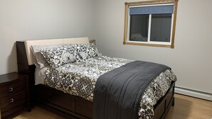 A bedroom with a bed, a nightstand, a dresser, and a window with a blue blind.