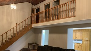 A spacious living area with a wooden staircase, a sofa, two armchairs, and a coffee table.
