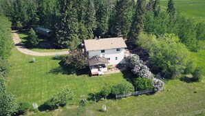 An aerial view of a single-story house with a fenced yard, surrounded by dense forest.