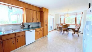 A kitchen with wooden cabinets, a dishwasher, and a dining area with wooden chairs and a table.