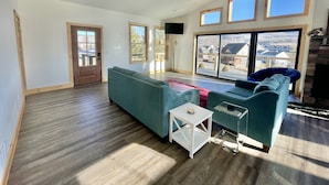 A spacious living room with a large sectional sofa, a small white side table, and a glass coffee table. There are three large windows providing a view of the outside. - Modern Cabin Facing Canaan Valley Ski Slopes (Davis)