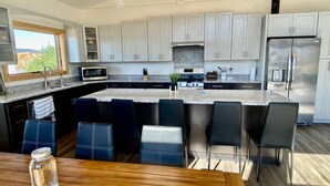 A modern kitchen with white cabinets, a stainless steel refrigerator, a microwave, and a gas stove. There are six bar stools and a wooden dining table. - Modern Cabin Facing Canaan Valley Ski Slopes (Davis)