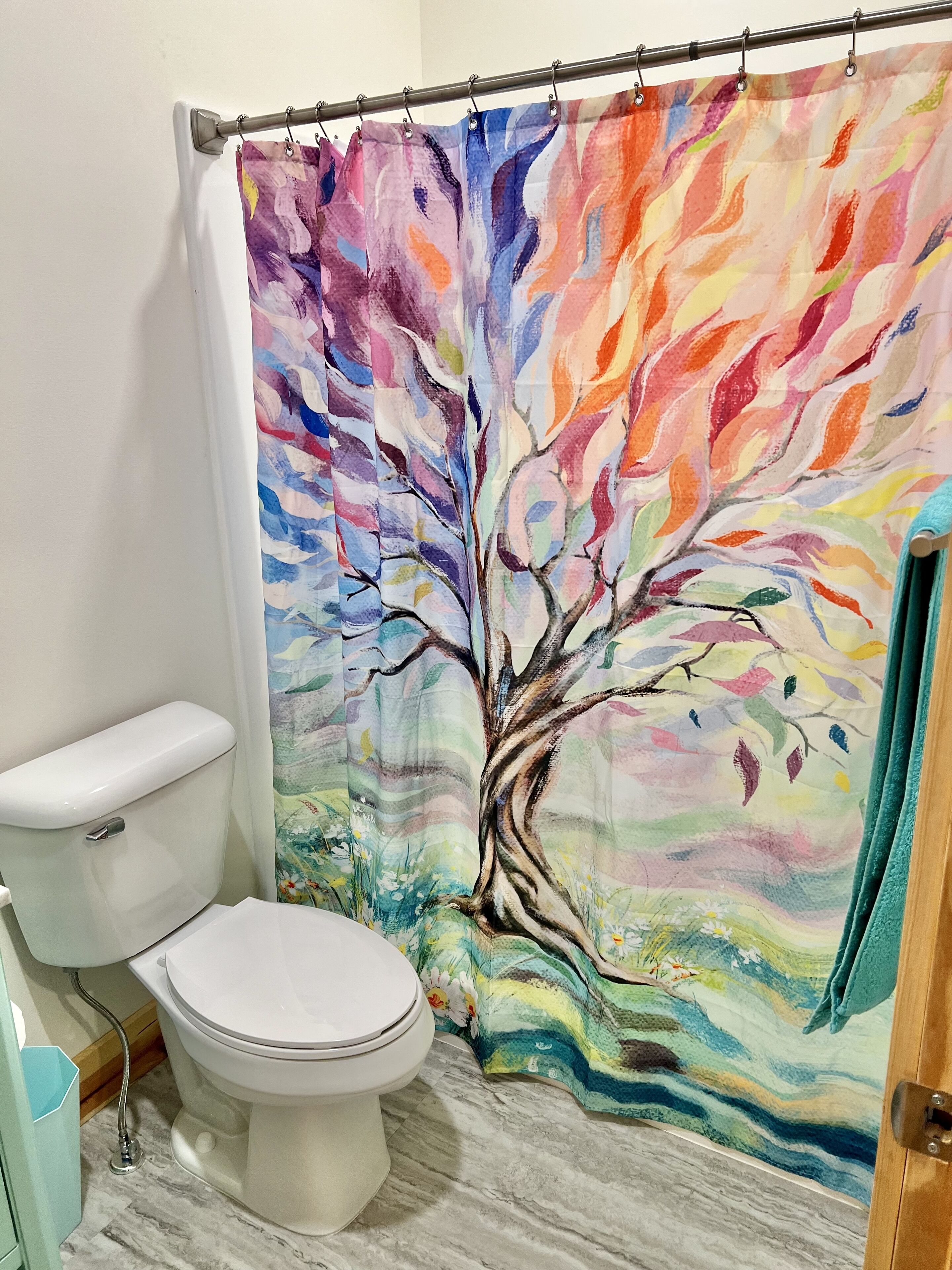 Une salle de bain avec des toilettes, un rideau de douche orné d’un motif d’arbre et un sol en marbre.