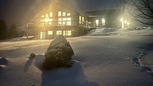 A snow-covered landscape with a large building featuring multiple windows and a balcony, illuminated by warm lights. - Modern Cabin Facing Canaan Valley Ski Slopes (Davis)