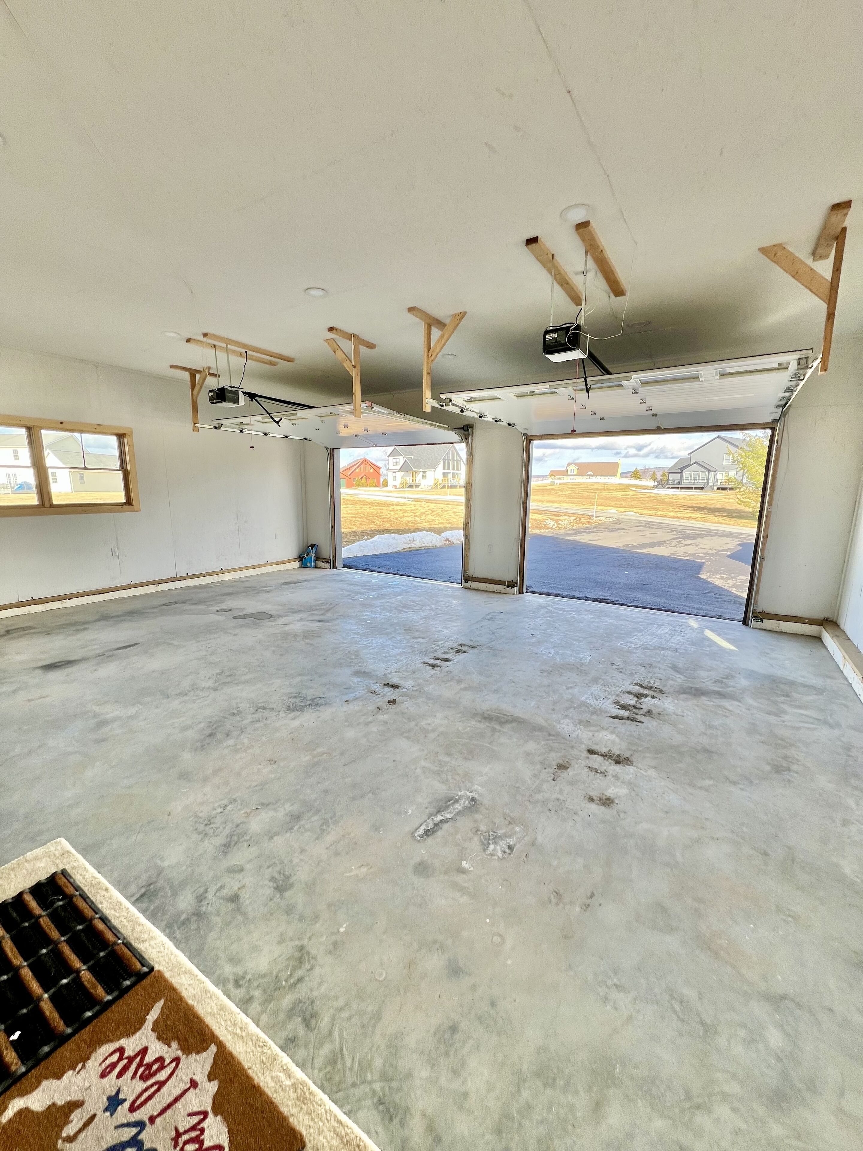 A large, unfinished interior space with a concrete floor, exposed ceiling beams, and a garage door.
