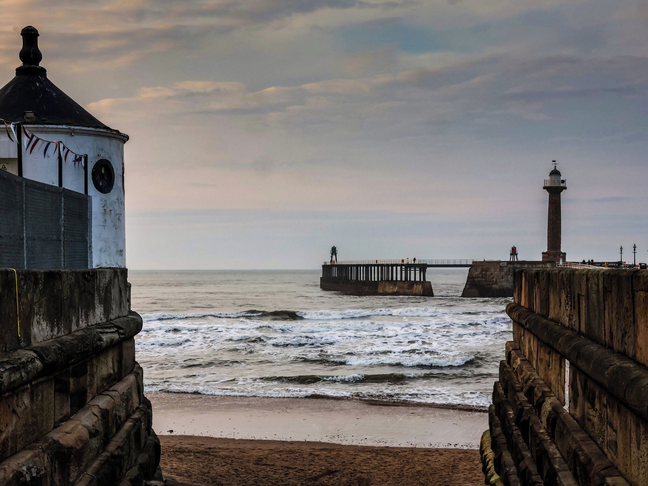 A coastal scene with a lighthouse, a pier, and a building with a circular window.
