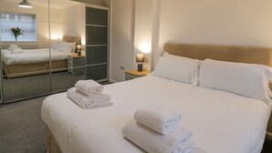 A hotel room with a large bed, a bedside table with a lamp, a mirror, and a wardrobe. - Whitby Haven (Whitby)