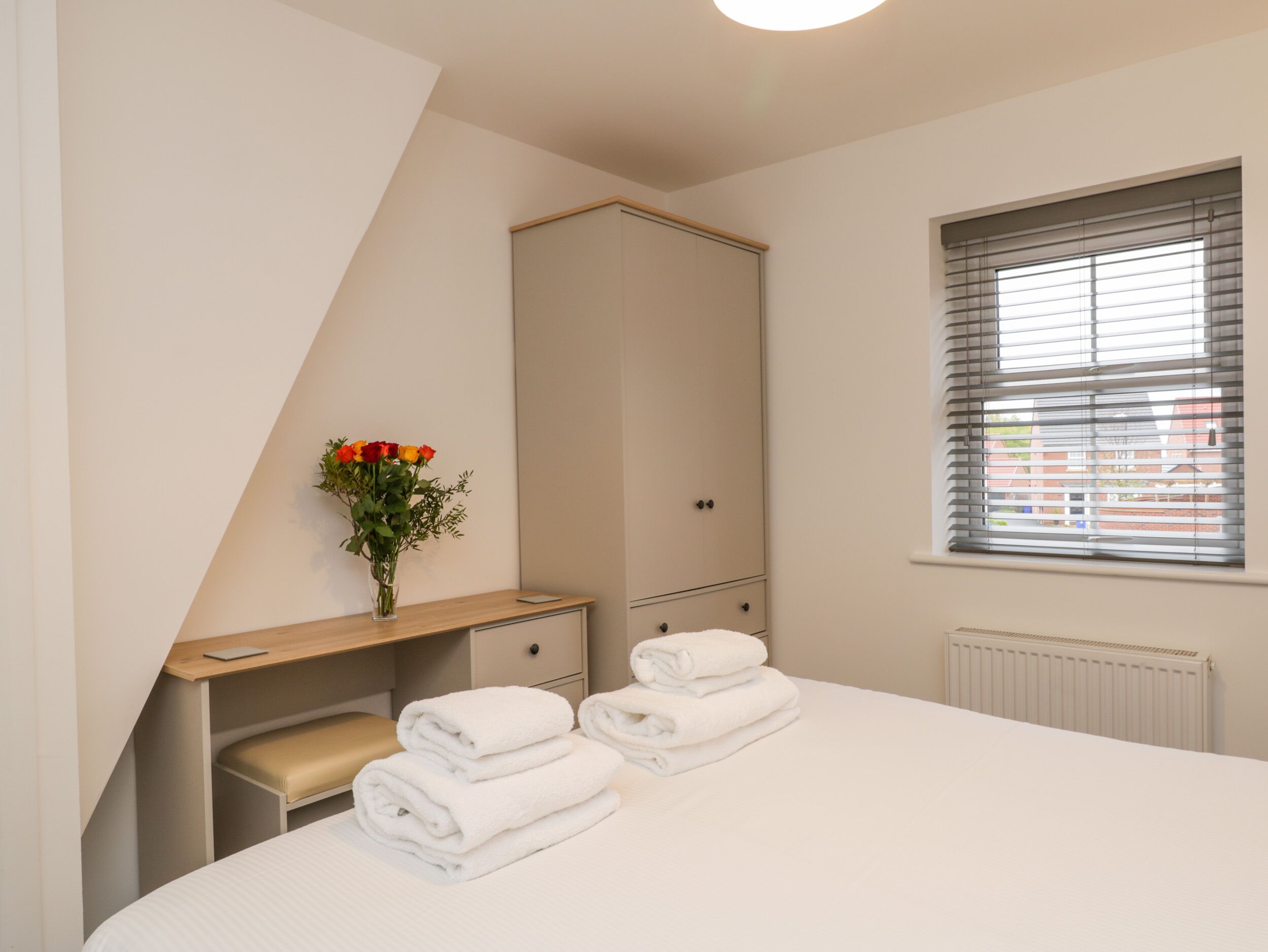 Een slaapkamer met een bed, een bureau, een kast en een raam met jaloezieën.