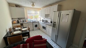 A compact kitchen with white cabinets, a stainless steel refrigerator, a washing machine, and a dining area with a table set for two. - Stunning 3-bed Apartment in Croydon (Croydon)