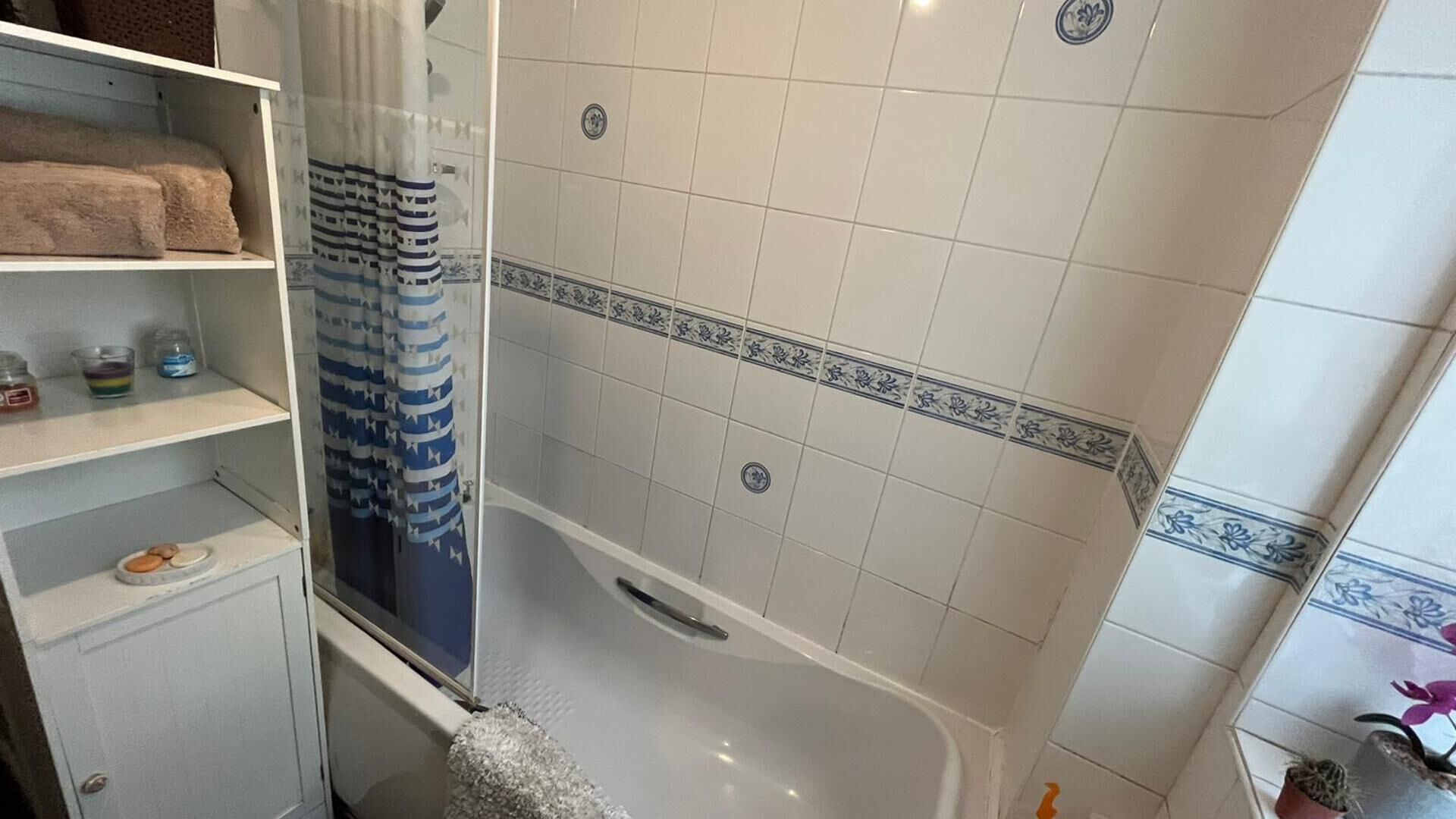 A bathroom with a bathtub, a shower curtain, and a tiled wall with a decorative border.