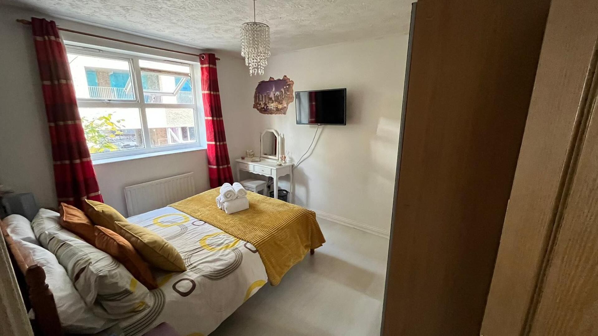A bedroom with a bed, a dresser, a mirror, a TV, and a window with curtains.