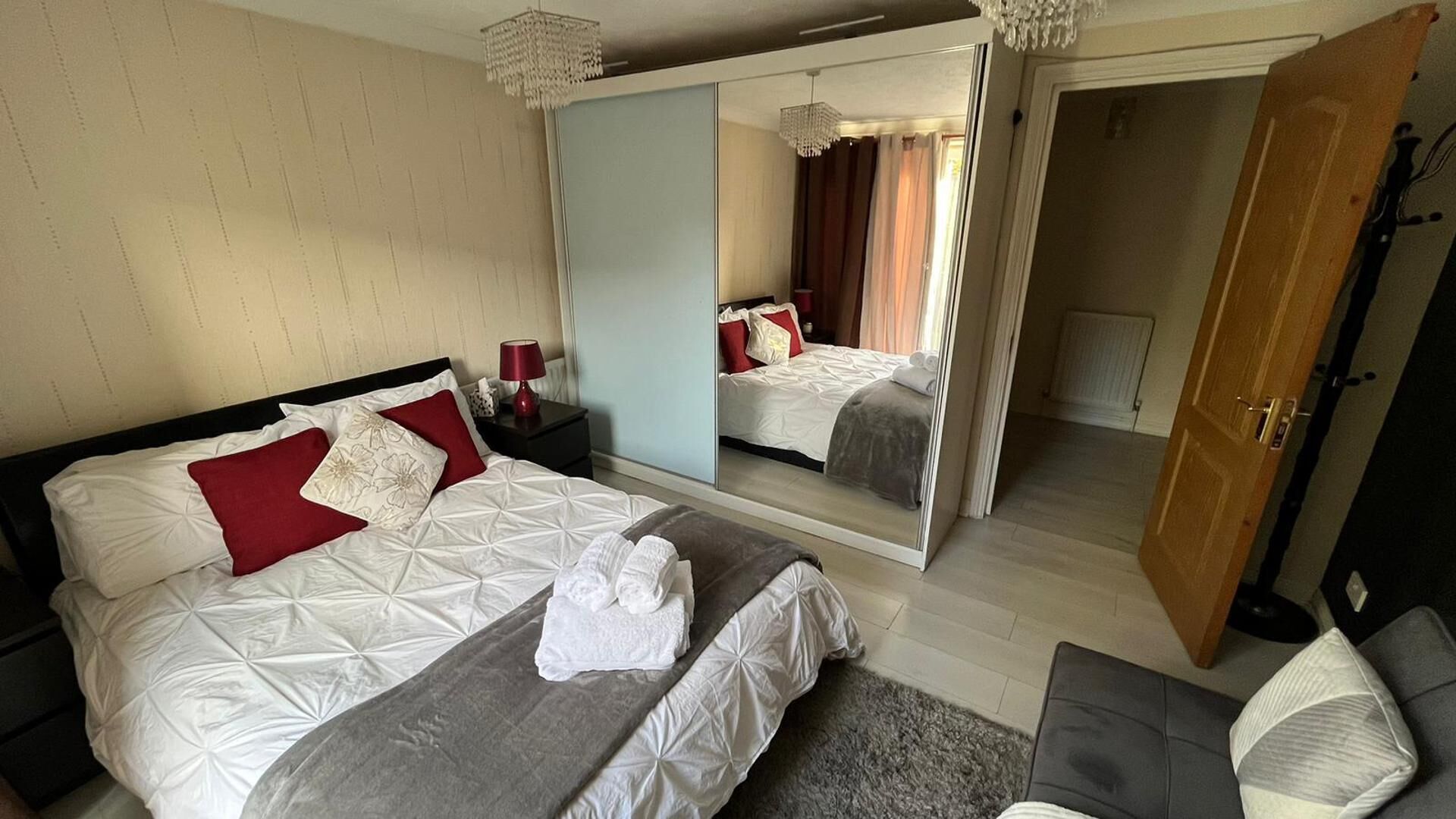 A hotel room with a large bed, a mirror, a bedside table, a chair, and a door.