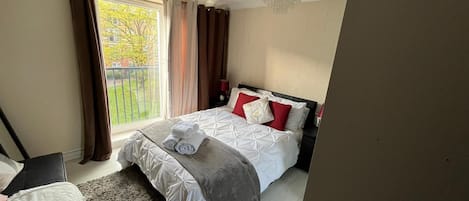 A hotel room with a bed, a window with curtains, a small table, and a chair.