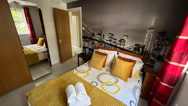 A hotel room with a bed, a mirror, a cityscape mural on the wall, and a red curtain. - Stunning 3-bed Apartment in Croydon (Croydon)