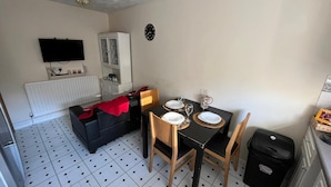 A compact living space with a dining area, a sofa, a cabinet, and a television on the wall. - Stunning 3-bed Apartment in Croydon (Croydon)