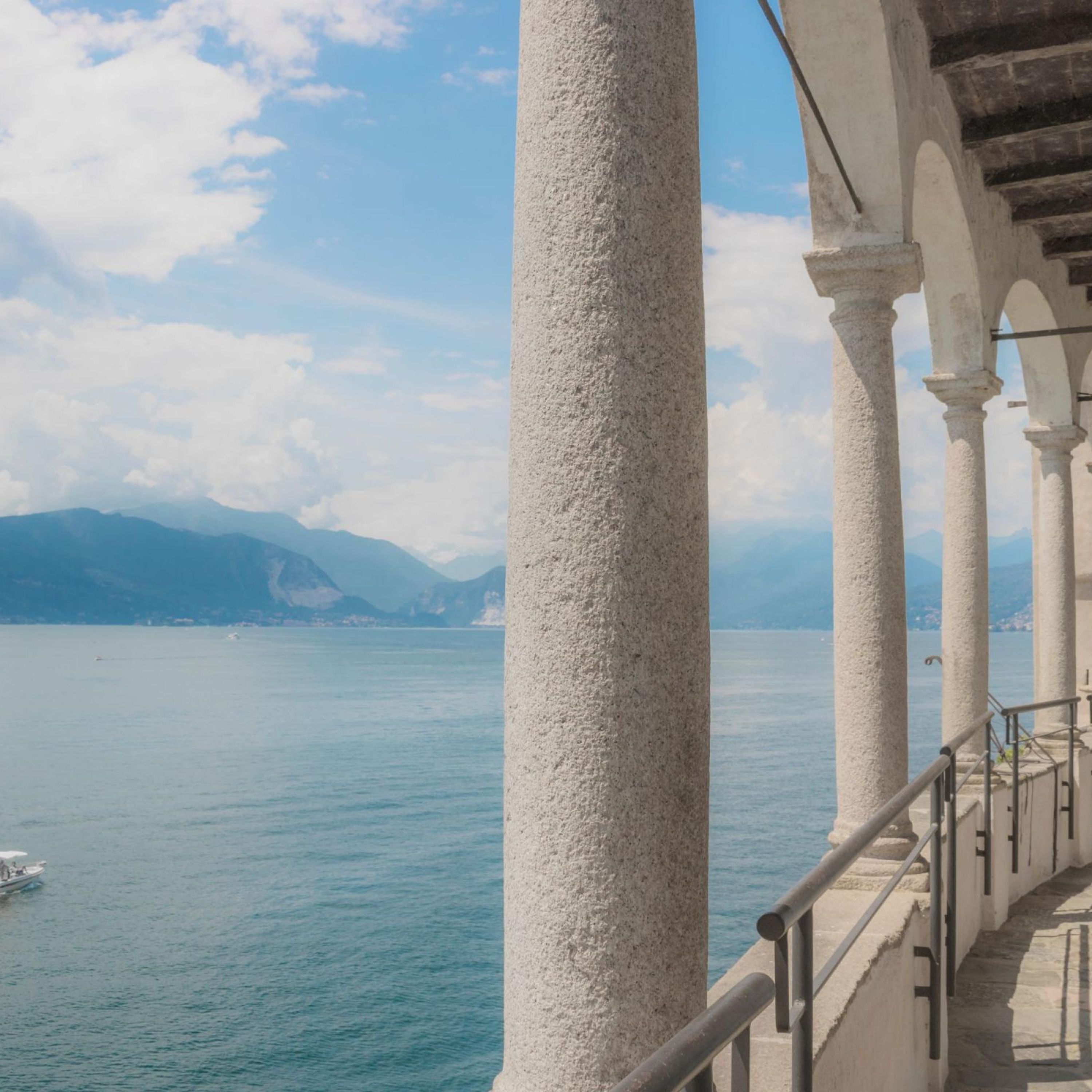 A seaside walkway with white columns and a view of the sea and mountains.