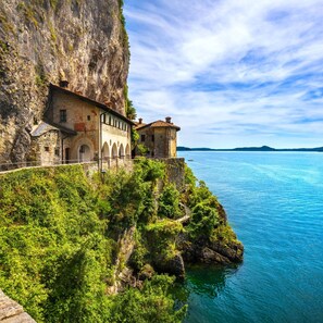 A coastal building with a stone facade, arched windows, and a balcony overlooking the sea. - Casa Amabile With Pool (Leggiuno)
