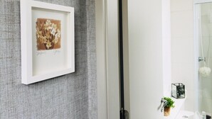 A framed artwork on a textured wall, a bathroom with a glass shower enclosure, and a sink with toiletries. - Av0806 Studio Avanhandava (São Paulo)