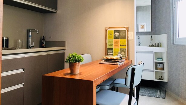 A modern kitchen with a wooden island, a potted plant, and a bulletin board with motivational quotes. - Av0806 Studio Avanhandava (São Paulo)