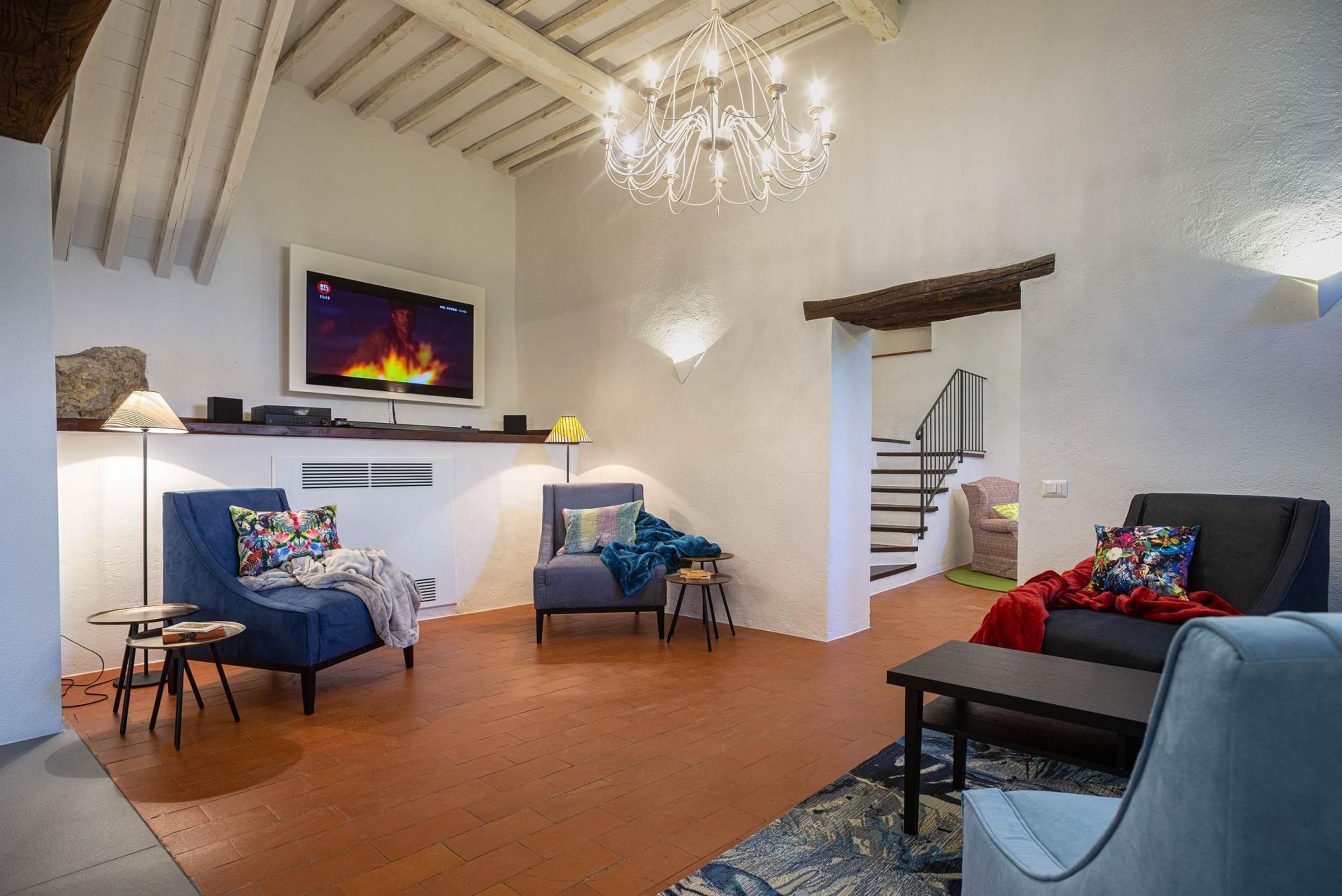 A modern living room with a flat-screen TV, a chandelier, and a staircase leading to another level.